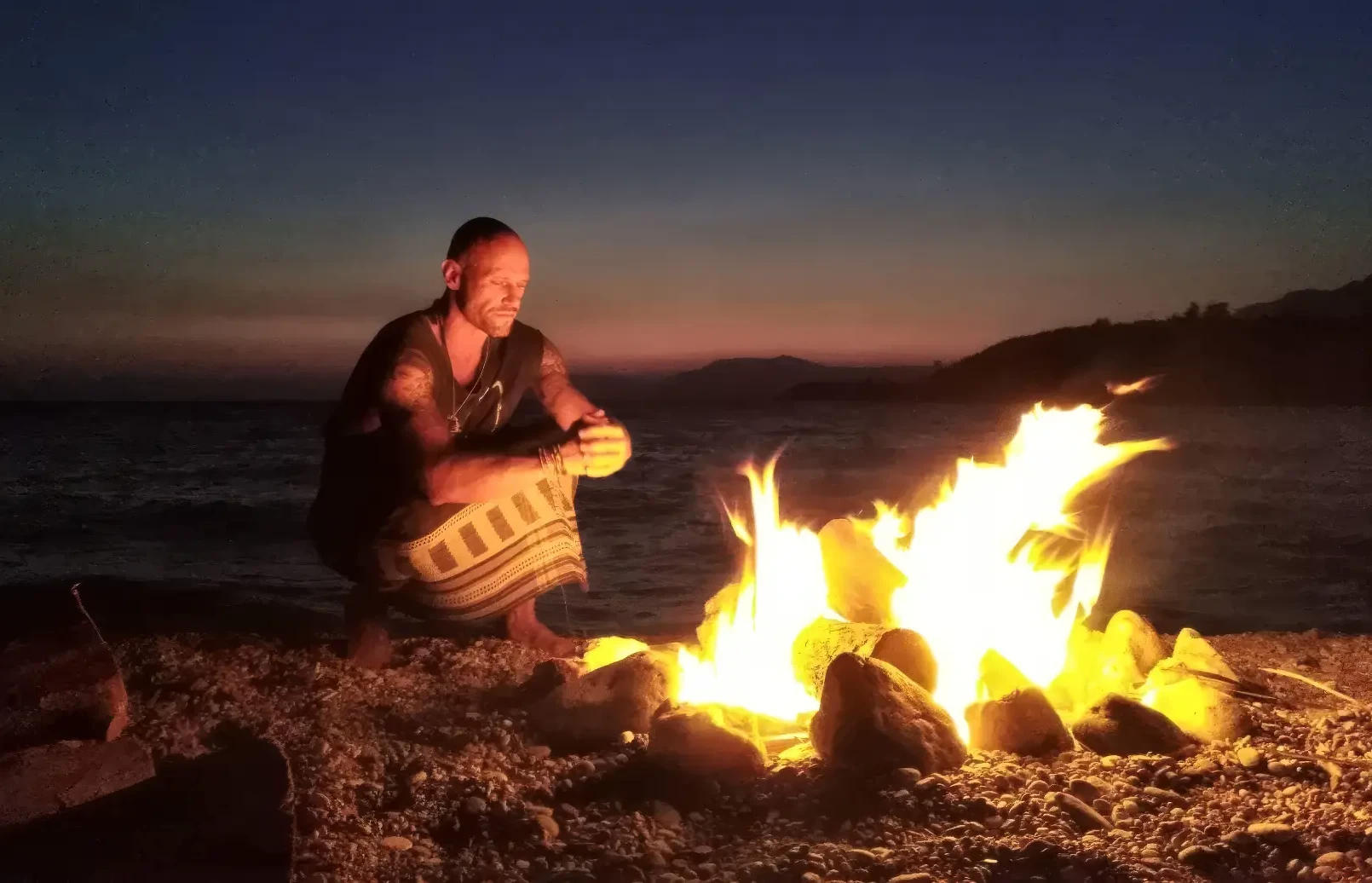 Jesse Kirley crouched beside a beach fire at dusk